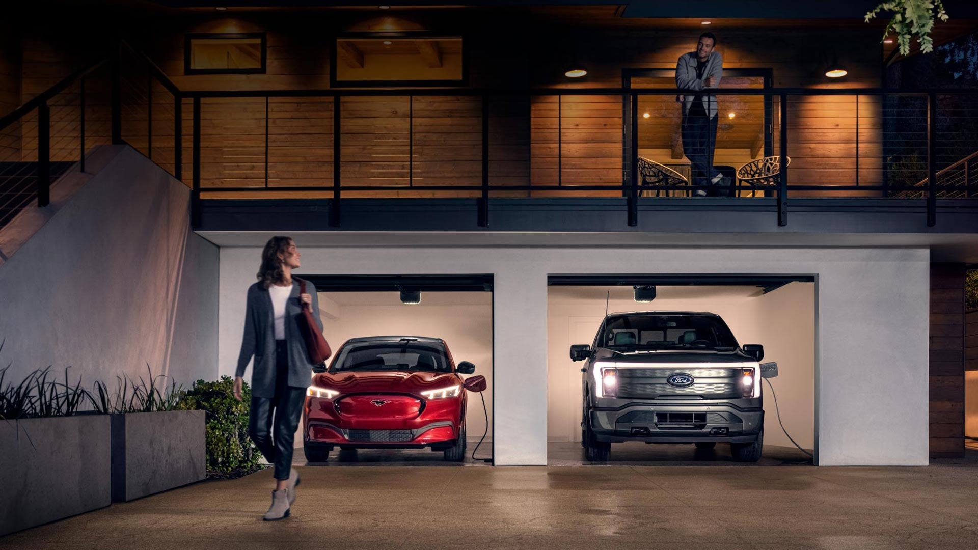 Woman walking out from home garage with a 2024 Mustang® Mach-E and Ford Lightning® truck in plugged-in and charging | Palm Coast Ford in Palm Coast FL